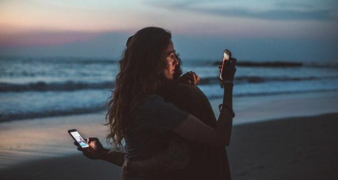 Ett par kramas och tittar på sina telefoner på stranden