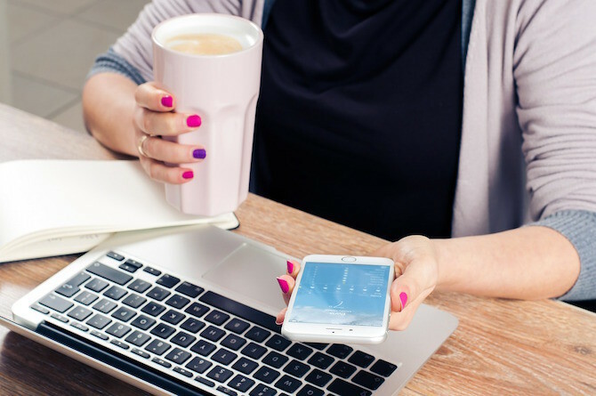 Kvinna som dricker kaffe på telefon och Mac